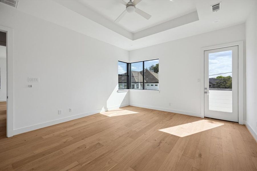 Primary bedroom with raised ceiling and corner windows.