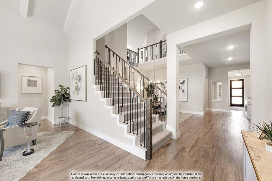 Two-story foyer with carpeted staircase, iron railings, hardwood floors, and open hallway leading to front door