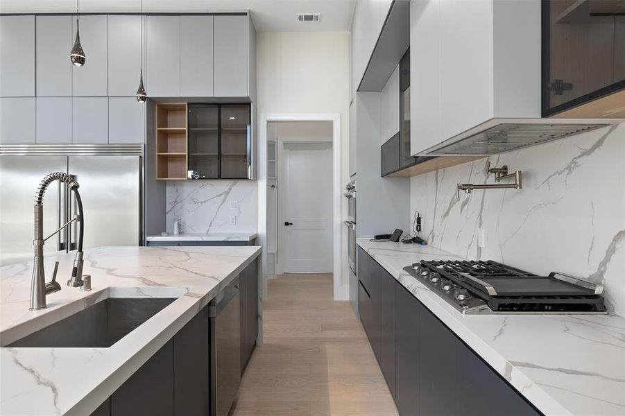 Kitchen featuring light hardwood / wood-style flooring, decorative light fixtures, sink, light stone countertops, and white cabinets