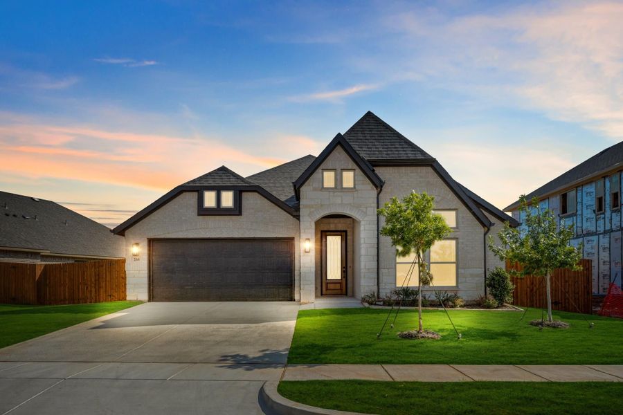 Single-story home with light stone exterior, dark roof, two-car garage, arched entry, and manicured lawn at dusk