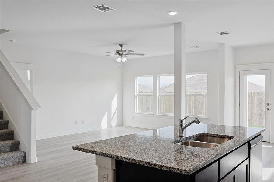 Kitchen with sink, ceiling fan, an island with sink, light hardwood / wood-style floors, and light stone counters