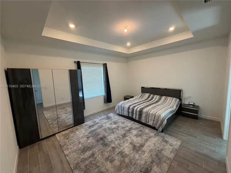 Tray ceiling featuring recessed lighting, wood-finish flooring, and a window with neutral blinds