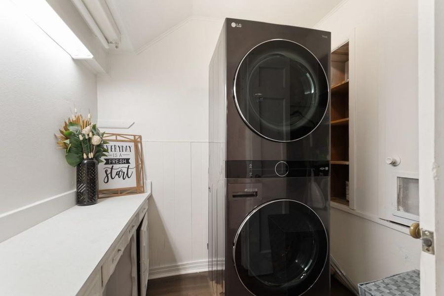 Clothes washing area with stacked washer and clothes dryer, dark wood-type flooring, and crown molding