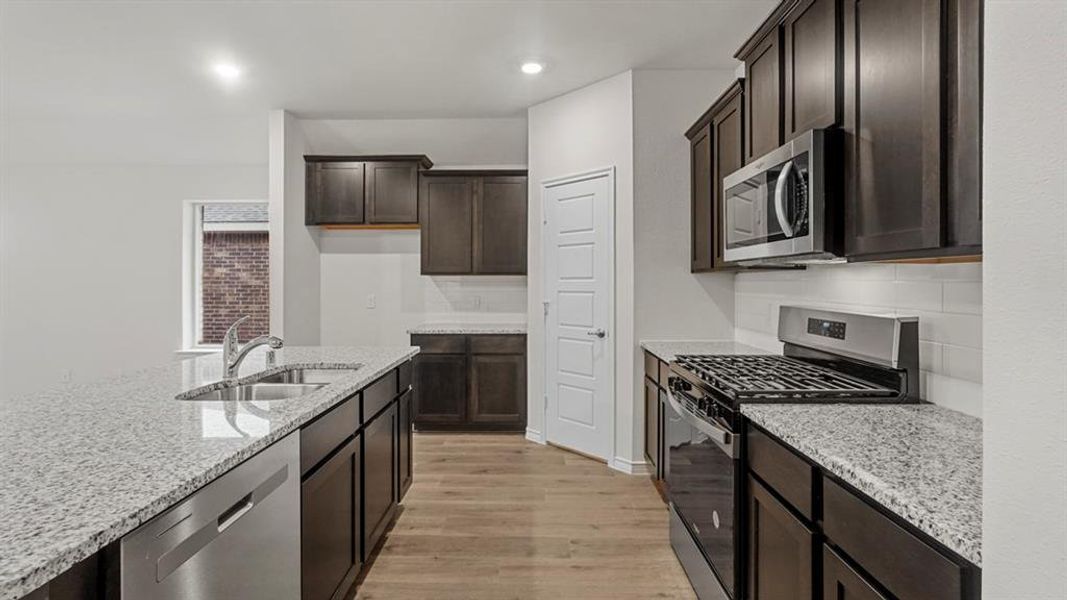 Kitchen featuring dark wood cabinetry, light granite countertops, stainless steel appliances, and wood-finish flooring