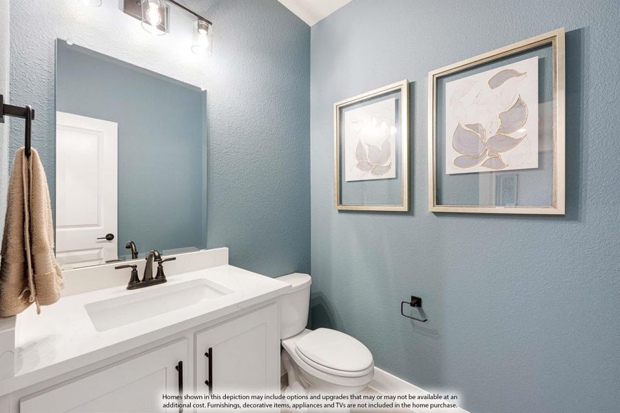 Powder room with white vanity, blue walls, large mirror, and two framed wall art pieces above toilet