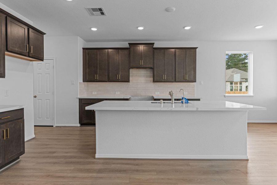 This light and bright kitchen features a large quartz island, dark stained cabinets, a large sink overlooking your family room, recessed lighting, and beautiful backsplash. This light and bright kitchen features a large quartz island, dark stained cabinets, a large sink overlooking your family room, recessed lighting, and beautiful backsplash.