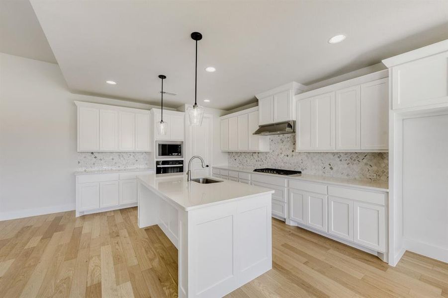 Kitchen with white cabinetry, light wood finished floors, and an island with sink