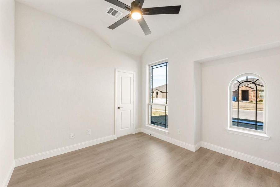 Empty bedroom with hardwood floors, ceiling fan, tall window, and arched accent window