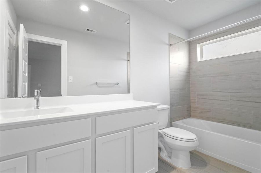 Secondary bath features tile flooring, bath/shower combo with tile surround, stained cabinets, beautiful light countertops, mirror, sleek fixtures and modern finishes.