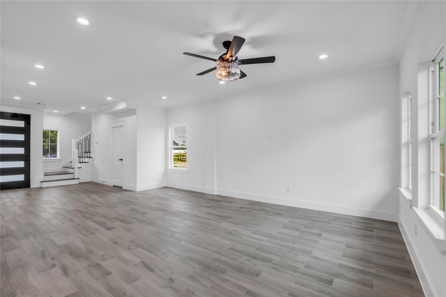 This inviting living room boasts sleek wood flooring, abundant natural light from large windows, and a stylish ceiling fan, creating a perfect blend of comfort and elegance.