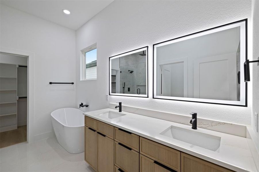 Full bath featuring a marble finish shower, a freestanding bath, double vanity, a walk in closet, and recessed lighting