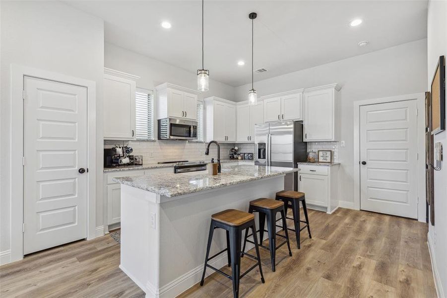 Kitchen featuring tasteful backsplash, stainless steel appliances, a center island with sink, light hardwood / wood-style floors, and white cabinetry