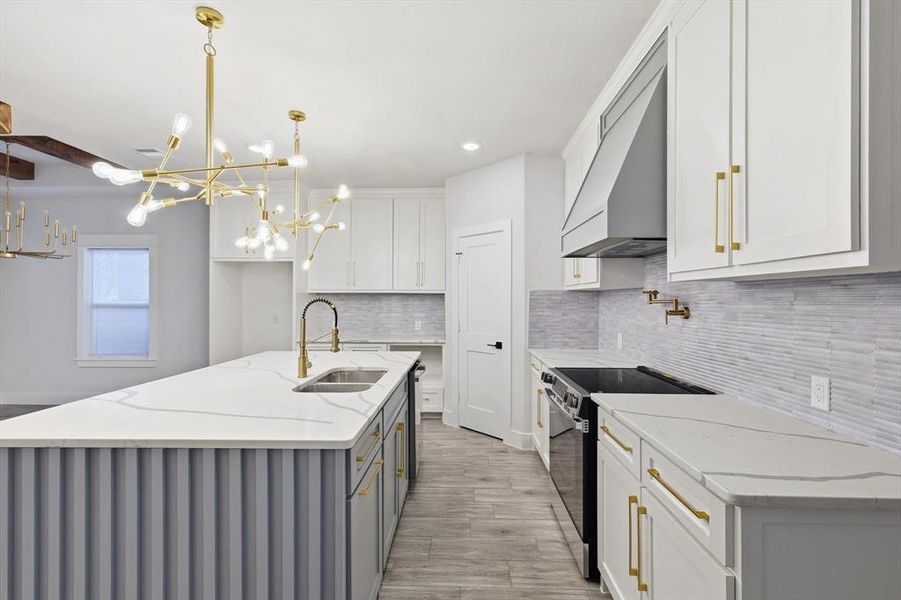 Kitchen featuring white cabinets, light stone counters, black / electric stove, pendant lighting, and a kitchen island with sink