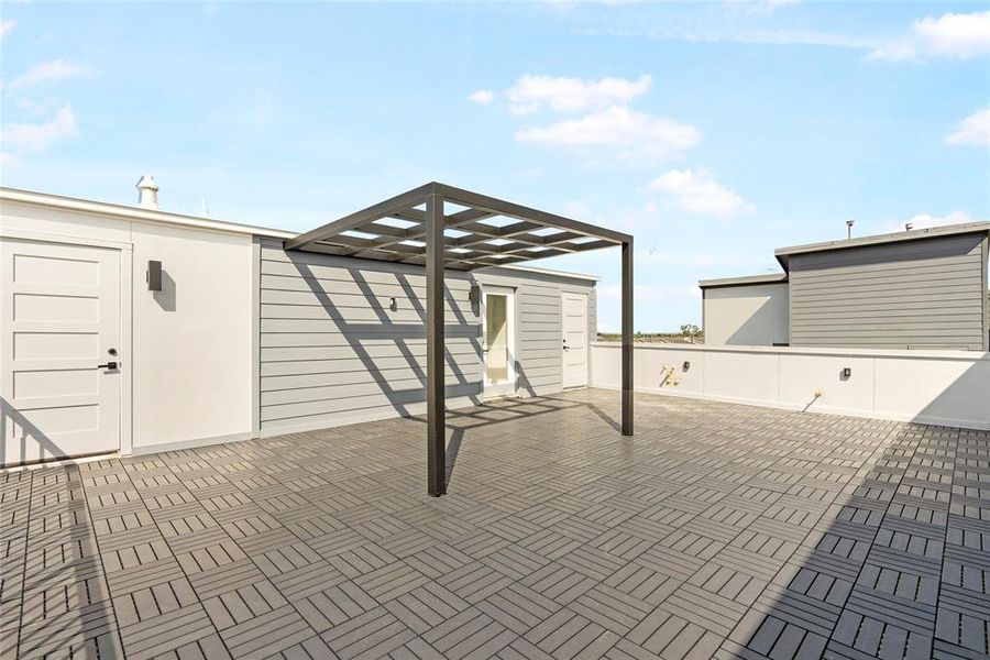 This is a spacious rooftop deck with a modern pergola, offering ample space for outdoor entertaining and relaxation. The area features a herringbone-patterned decked floor and is surrounded by a low privacy wall with lighting.