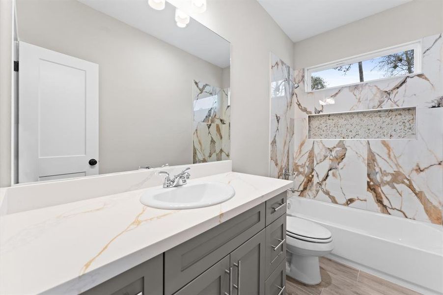 This bathroom features a modern design with a spacious vanity, marble-patterned tiles in the shower, and a large mirror. Bright and airy, it offers a clean, stylish look.