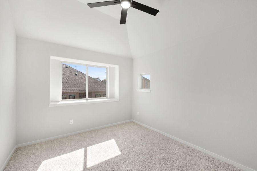 Empty bedroom with vaulted ceiling, ceiling fan, carpet flooring, and two windows Empty bedroom with vaulted ceiling, ceiling fan, carpet flooring, and two windows