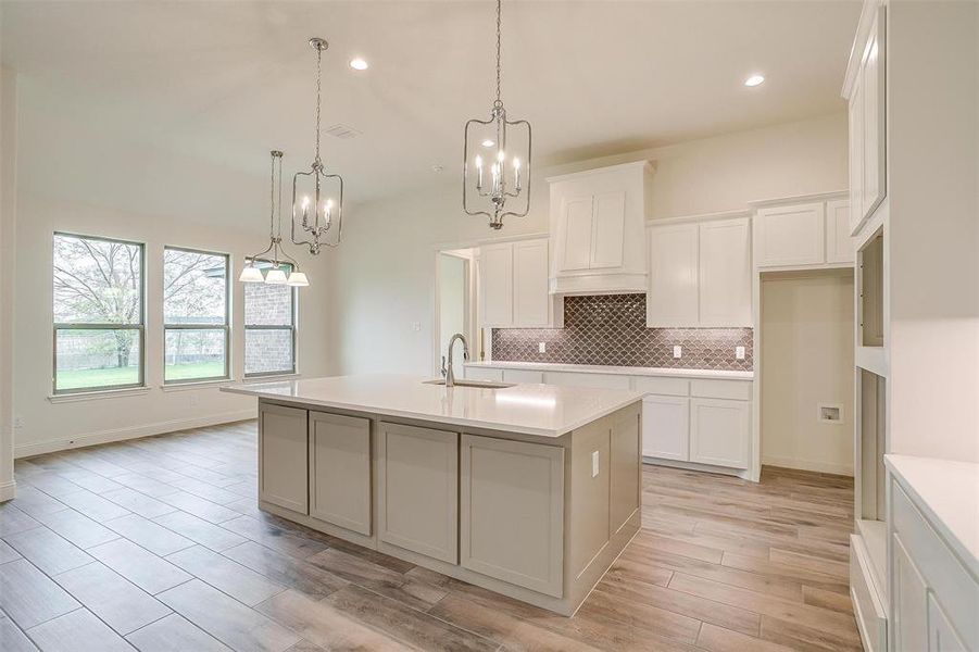 Kitchen featuring sink, decorative light fixtures, a center island with sink, and light hardwood / wood-style flooring