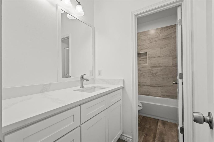 Full bathroom with tiled shower / bath, vanity, wood-type flooring, and toilet