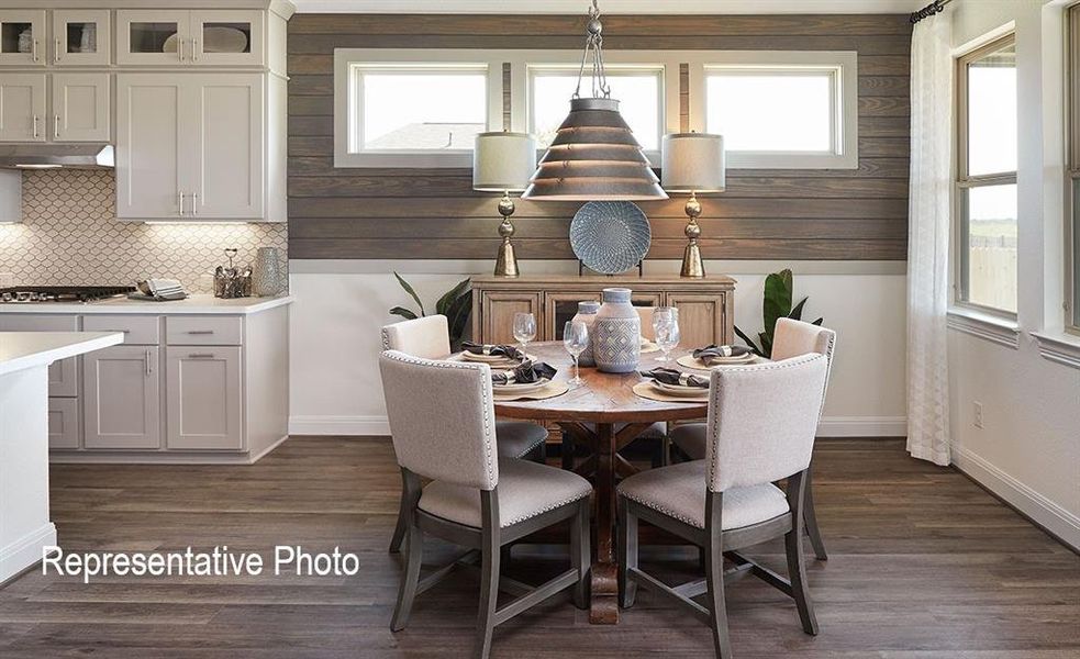 Open-concept interior featuring wood-finish flooring, a kitchen with light-toned cabinetry and a tiled backsplash, a dining area with a wood panel accent wall, and multiple windows