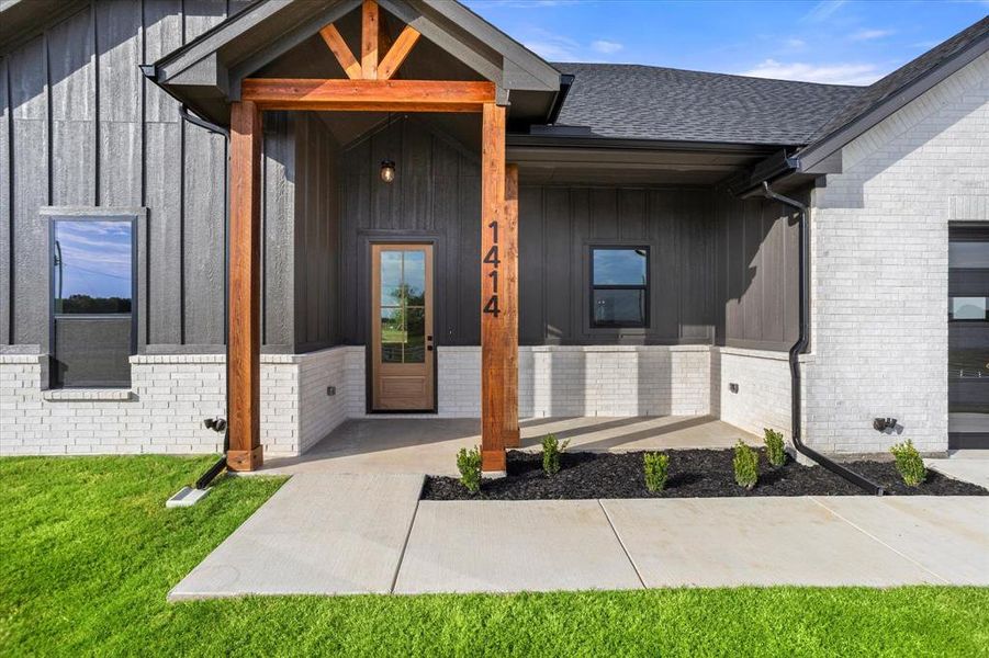 Doorway to property featuring board and batten siding, brick siding, a porch, and roof with shingles Doorway to property featuring board and batten siding, brick siding, a porch, and roof with shingles