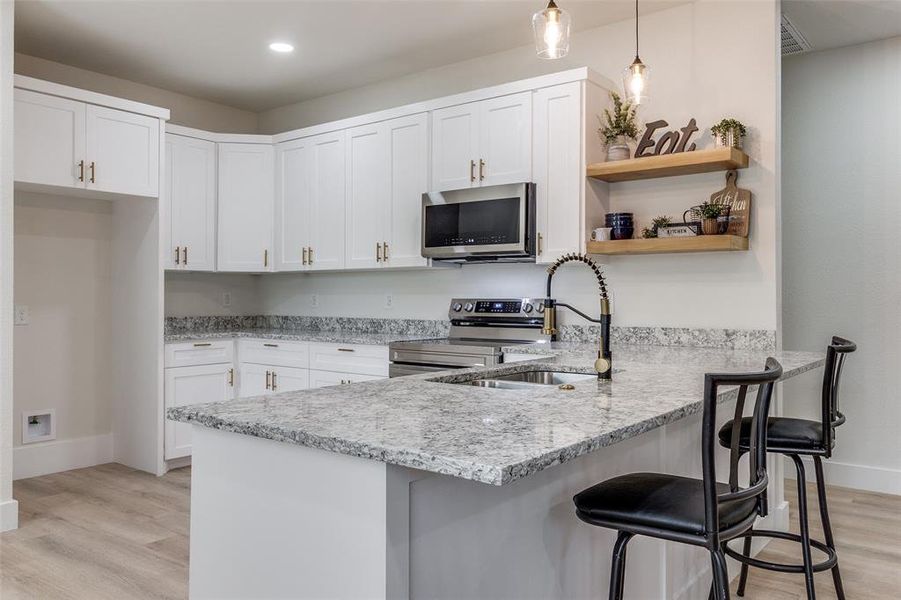 Kitchen with decorative light fixtures, appliances with stainless steel finishes, light wood-type flooring, and kitchen peninsula