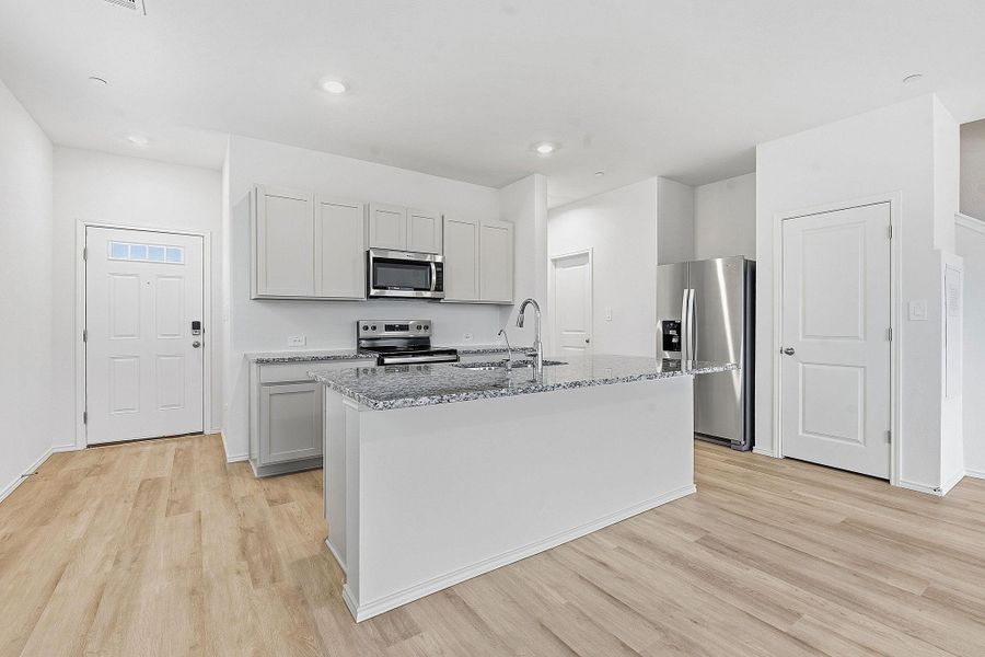 Open-concept kitchen featuring light wood-finish flooring, a central island with a sink and a granite-style countertop, light-toned cabinetry, stainless steel appliances, and a recessed lighting system Open-concept kitchen featuring light wood-finish flooring, a central island with a sink and a granite-style countertop, light-toned cabinetry, stainless steel appliances, and a recessed lighting system