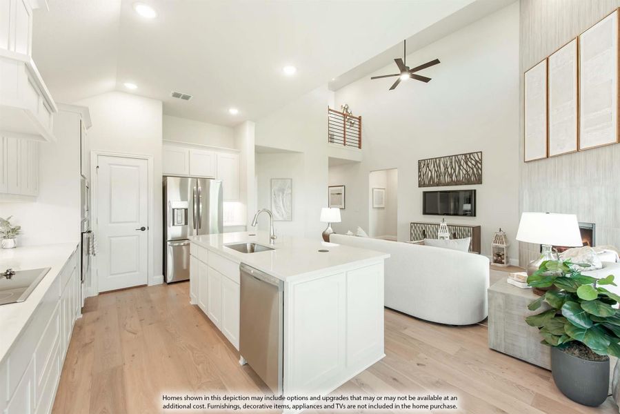 Open-concept kitchen with white island, stainless appliances, and light wood floors flowing into living room with high ceilings