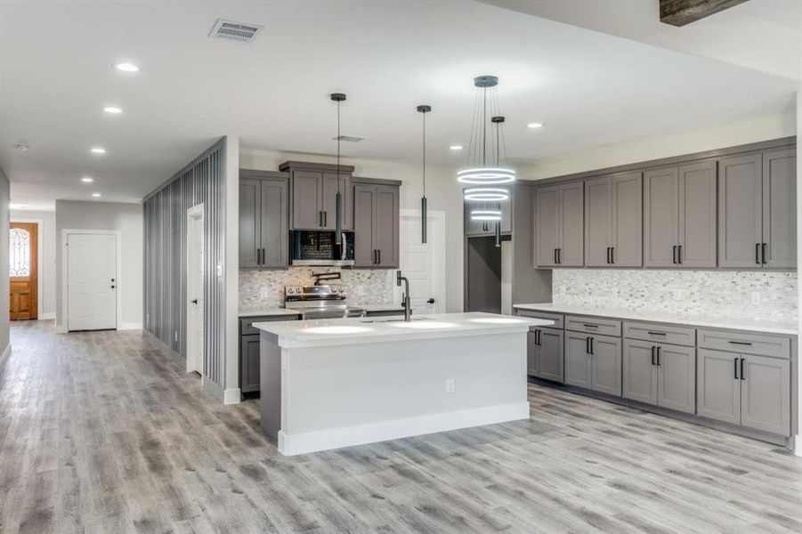 Kitchen featuring pendant lighting, gray cabinetry, backsplash, light wood-type flooring, and stainless steel appliances