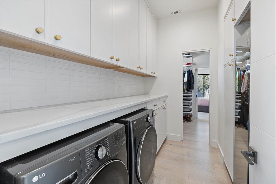 Washroom with light wood-type flooring, washing machine and clothes dryer, and cabinet space