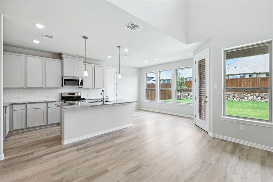 Kitchen featuring appliances with stainless steel finishes, light wood-type flooring, light stone counters, tasteful backsplash, and pendant lighting Kitchen featuring appliances with stainless steel finishes, light wood-type flooring, light stone counters, tasteful backsplash, and pendant lighting