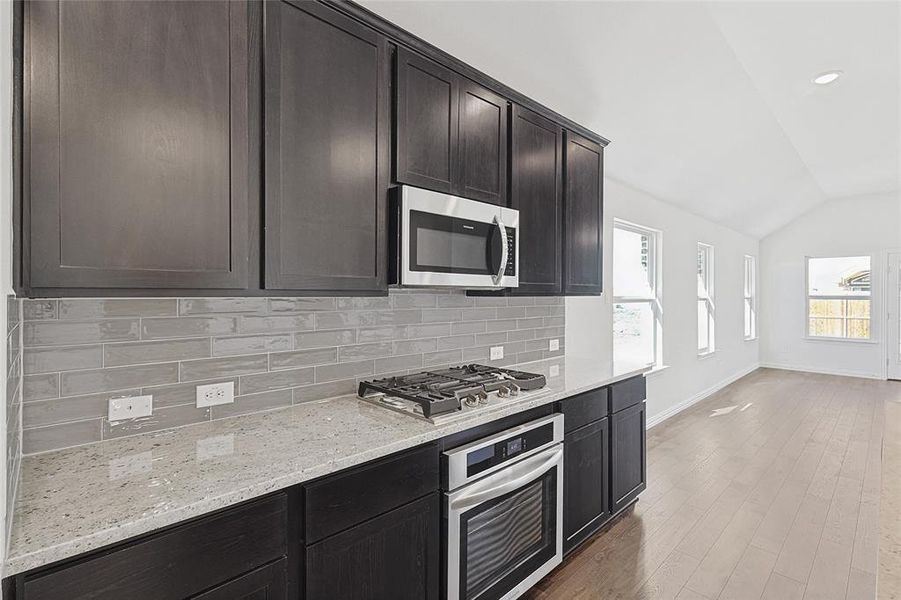 Kitchen featuring light stone countertops, backsplash, stainless steel appliances, vaulted ceiling, and hardwood / wood-style flooring