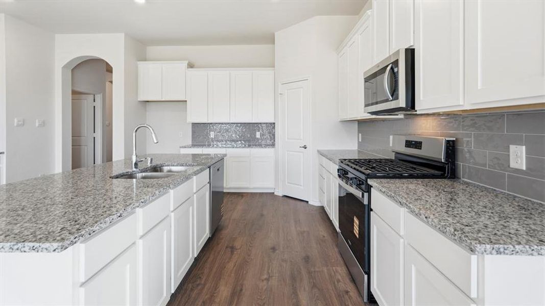 Kitchen featuring appliances with stainless steel finishes, white cabinets, an island with sink, and dark wood-style floors Kitchen featuring appliances with stainless steel finishes, white cabinets, an island with sink, and dark wood-style floors