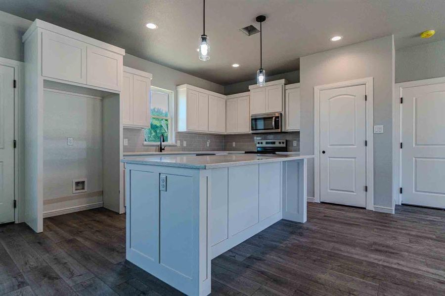 Kitchen featuring white cabinetry, a center island, dark wood-style floors, tasteful backsplash, and appliances with stainless steel finishes Kitchen featuring white cabinetry, a center island, dark wood-style floors, tasteful backsplash, and appliances with stainless steel finishes