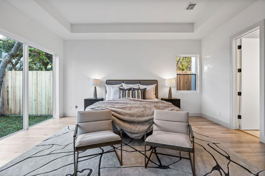 Bedroom featuring a tray ceiling, multiple windows, light hardwood / wood-style floors, and access to exterior