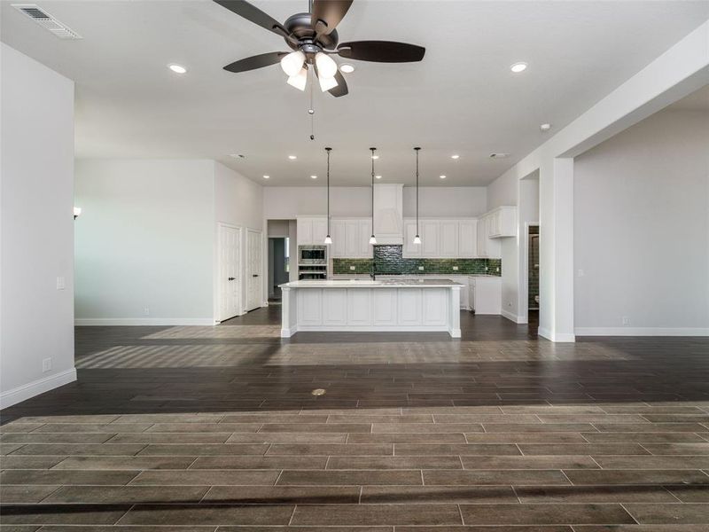Kitchen featuring backsplash, white cabinets, ceiling fan, open floor plan, and decorative light fixtures