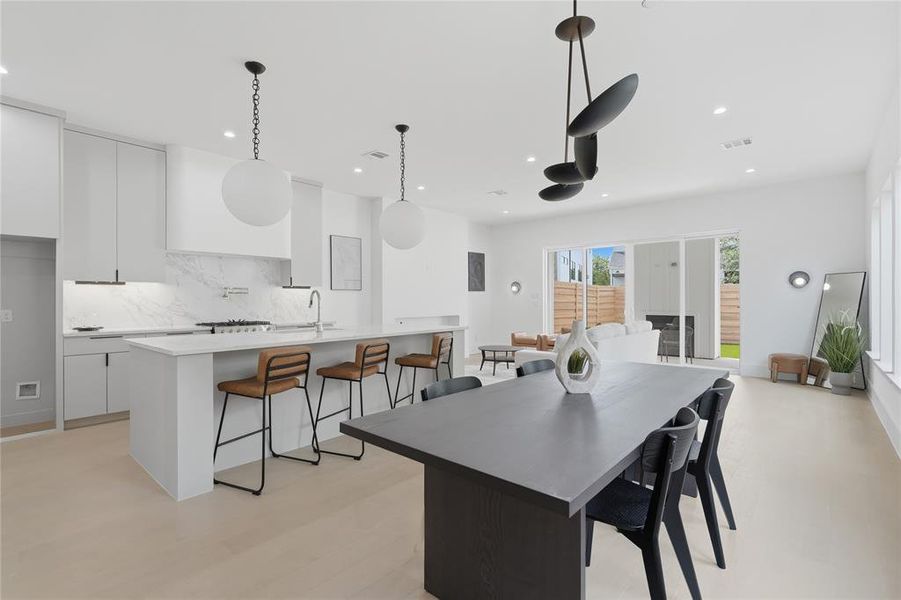 Open-concept living area featuring a kitchen island with seating, white shaker cabinetry, a gas range with a marble-patterned backsplash, and light wood-finish flooring