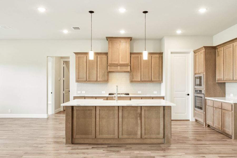 Kitchen with large center island, wood cabinets, white countertops, pendant lights, and light hardwood floors Kitchen with large center island, wood cabinets, white countertops, pendant lights, and light hardwood floors