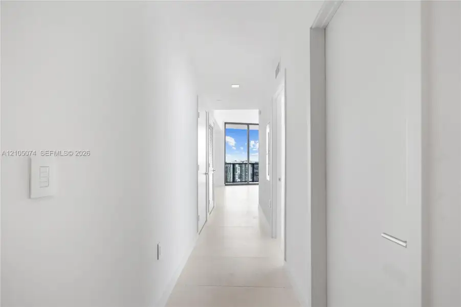 Hallway featuring neutral-toned tile flooring, recessed ceiling lighting, and floor-to-ceiling glass sliding doors
