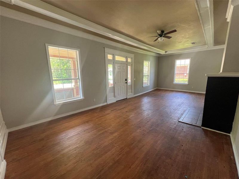 Unfurnished living room with a raised ceiling, dark wood-style floors, a ceiling fan, and ornamental molding Unfurnished living room with a raised ceiling, dark wood-style floors, a ceiling fan, and ornamental molding