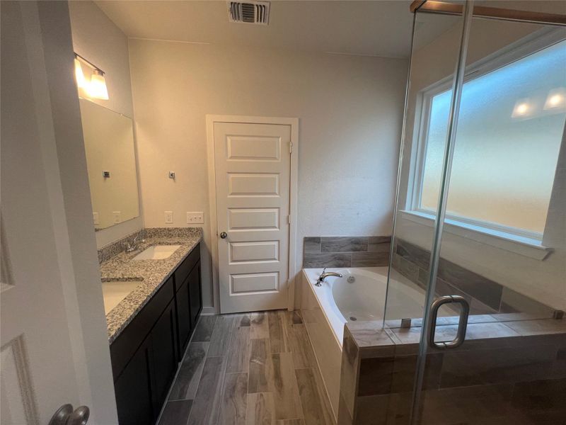 Luxurious primary bathroom featuring a double vanity with stone counters, a separate soaking tub, and a glass-enclosed shower.