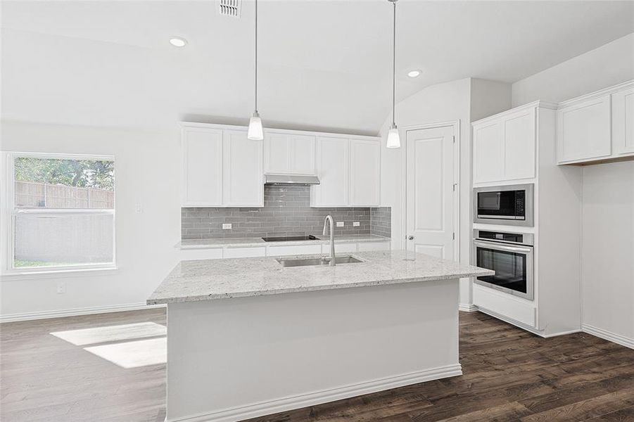 Kitchen with white cabinets, stainless steel appliances, dark wood-type flooring, and an island with sink