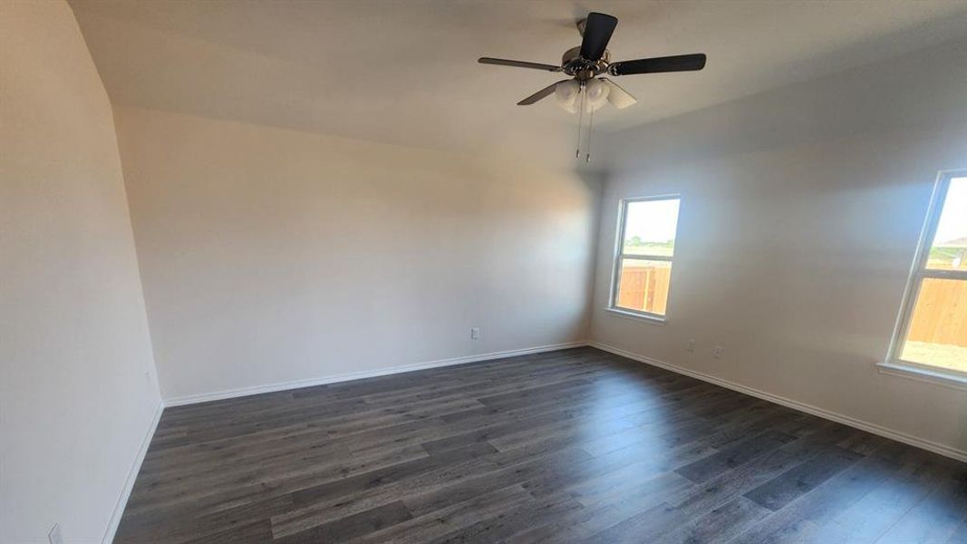 Spacious interior room featuring wood-finish flooring, neutral wall tones, multiple windows, a ceiling fan with integrated lighting, and white baseboards Spacious interior room featuring wood-finish flooring, neutral wall tones, multiple windows, a ceiling fan with integrated lighting, and white baseboards