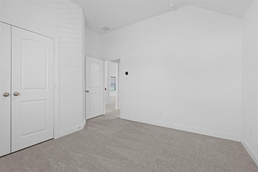 Unfurnished bedroom featuring light carpet, a closet, and vaulted ceiling