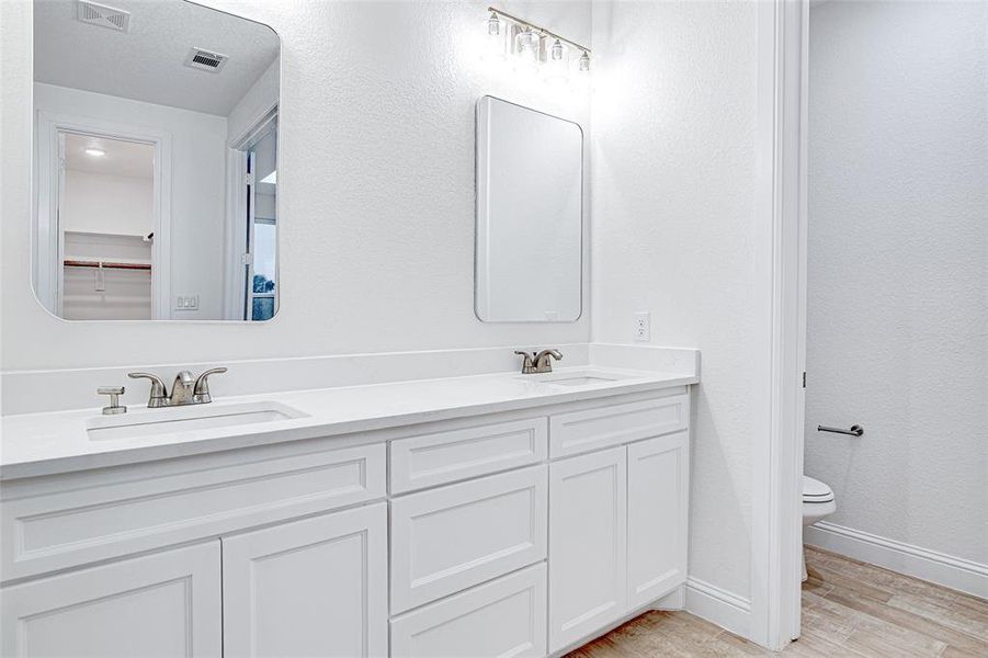 Full bathroom featuring wood finished floors, toilet, baseboards, and double vanity Full bathroom featuring wood finished floors, toilet, baseboards, and double vanity