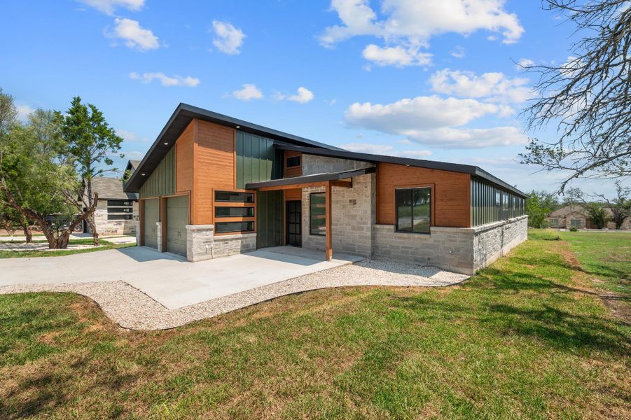 Rear view of property featuring stone siding, a lawn, a garage, and concrete driveway Rear view of property featuring stone siding, a lawn, a garage, and concrete driveway
