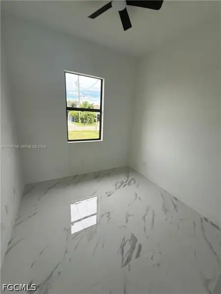 Interior room featuring large-format stone-patterned floor tile, neutral wall paint, and a matte black ceiling fan