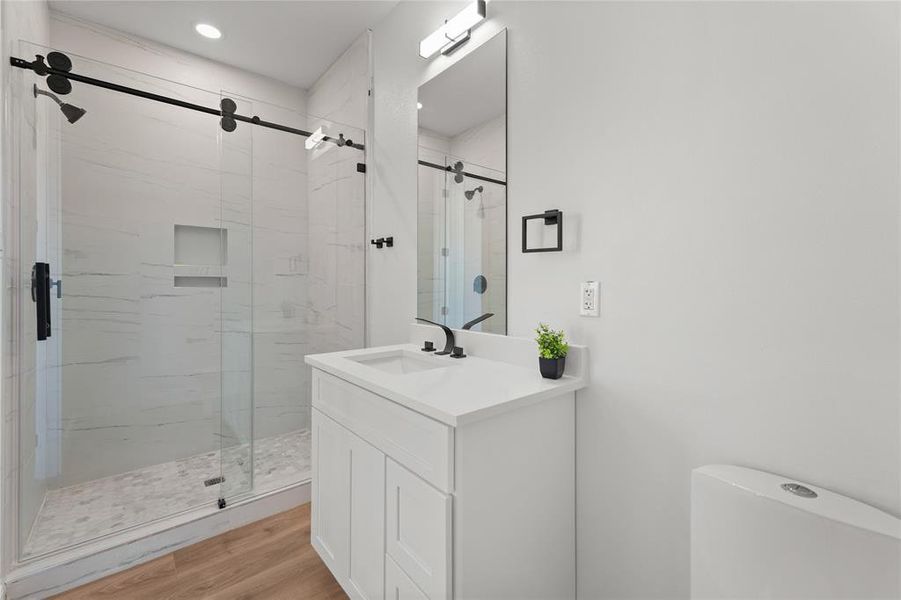 Bathroom featuring a marble finish shower, vanity, and light wood-type flooring