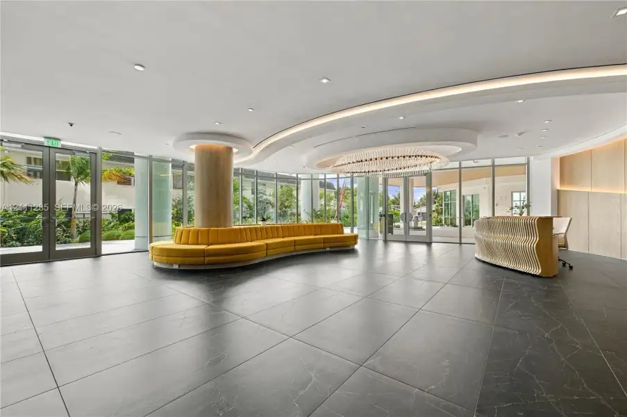 Lobby featuring large-format dark stone flooring, floor-to-ceiling glass walls, recessed cove lighting, and a circular chandelier Lobby featuring large-format dark stone flooring, floor-to-ceiling glass walls, recessed cove lighting, and a circular chandelier