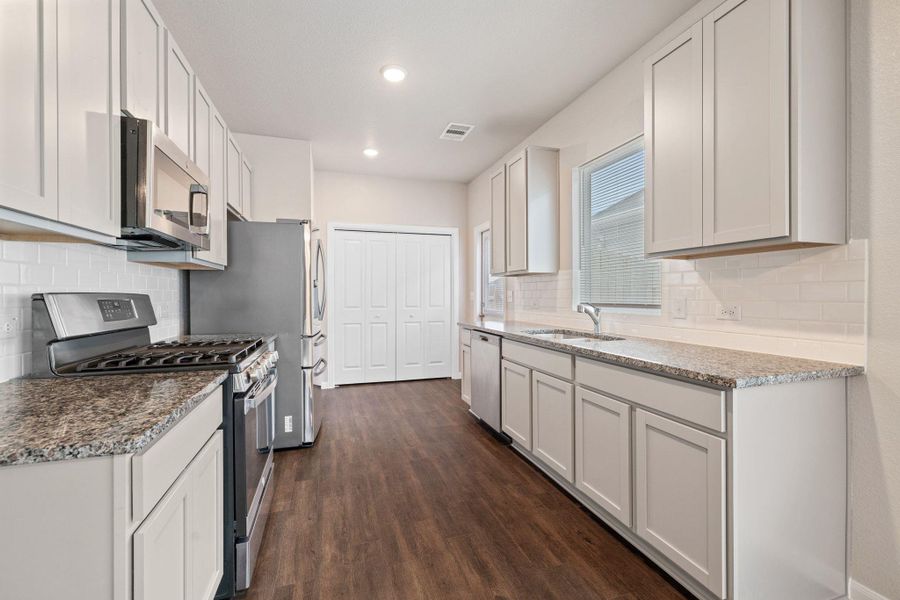 Kitchen with appliances with stainless steel finishes, backsplash, light stone counters, dark wood-style flooring, and white cabinetry