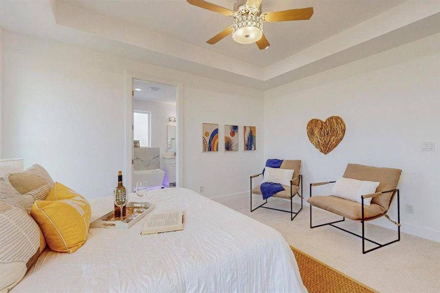 Bedroom featuring ceiling fan, a raised ceiling, connected bathroom, and light carpet